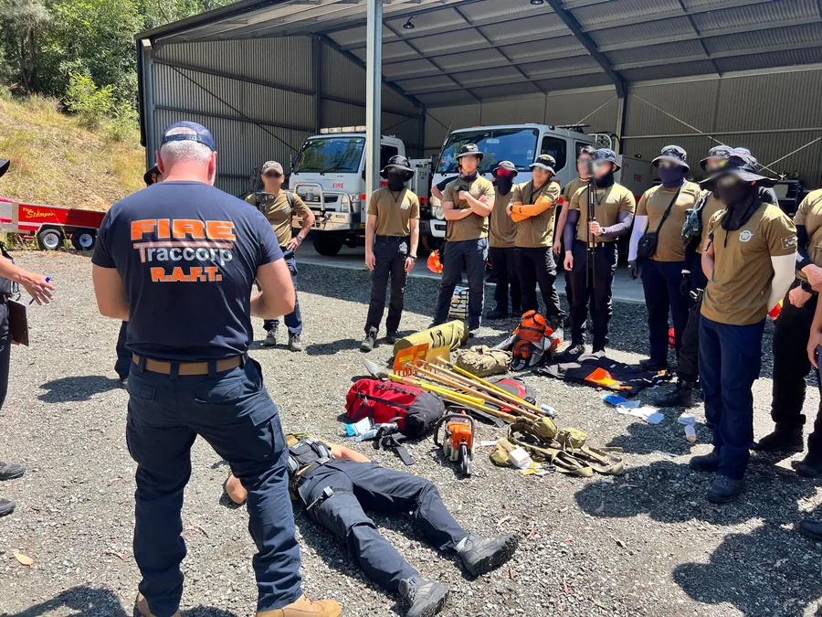Instructor briefing a training group in front of the engine bay, with equipment laid out on the ground